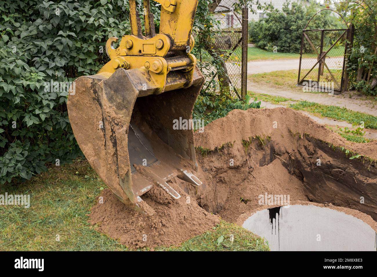 Un cubo de excavadora con un montón de arena y tierra entierra anillos de hormigón en la zona industrial. Foto de stock