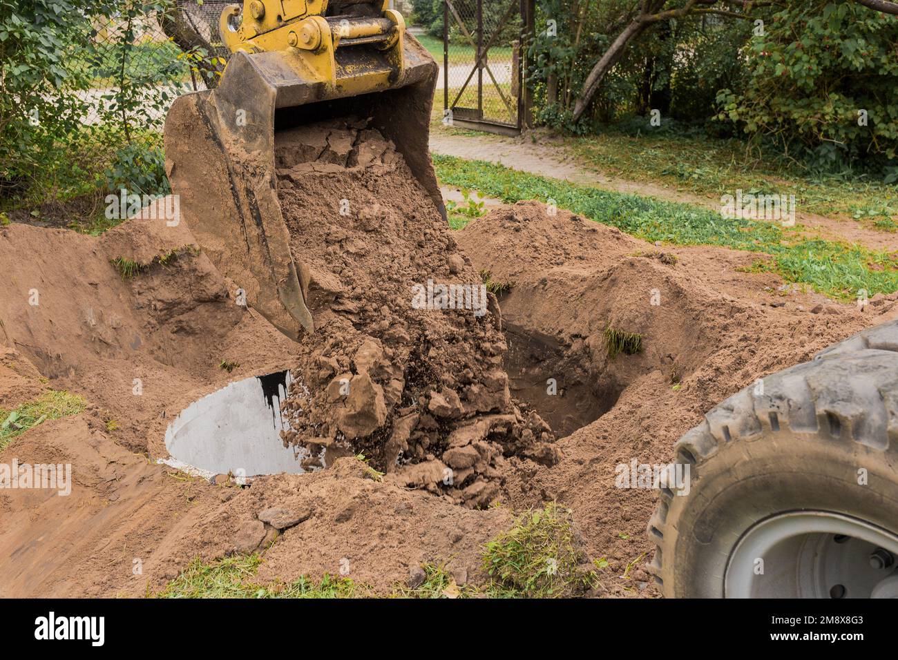 Un cubo de excavadora con un montón de arena y tierra entierra anillos de hormigón en la zona industrial. Foto de stock