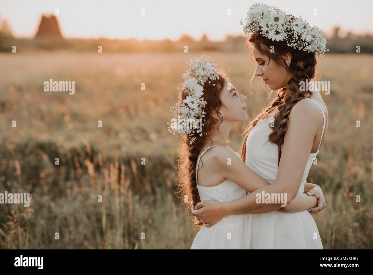 madre e hija abrazándose juntos en vestidos blancos con trenzas y coronas florales en estilo boho en verano al atardecer en el campo. Añadido un pequeño gra Fotografía de stock - Alamy madre e hija abrazándose juntos en vestidos blancos con trenzas y coronas florales en estilo boho en verano al atardecer en el campo. Añadido un pequeño gra Fotografía de stock - Alamy