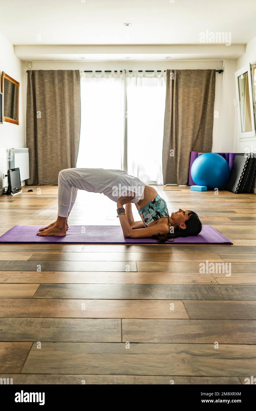 Vista lateral de una mujer practicando yoga, haciendo pose de puente (Setu Bandha Sarvangasana) Foto de stock