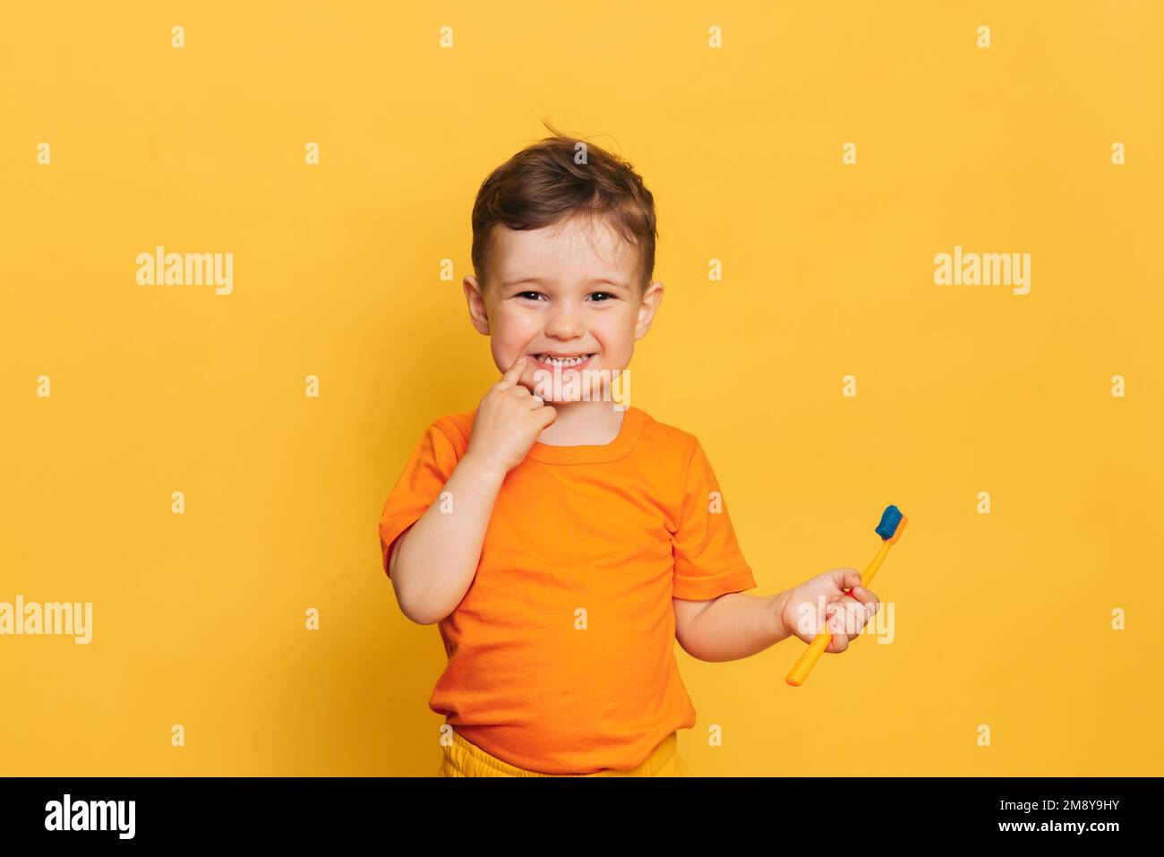 Niño bebé feliz cepillando sus dientes con cepillo de dientes sobre un fondo amarillo. Cuidado de la salud, higiene oral. Foto de stock