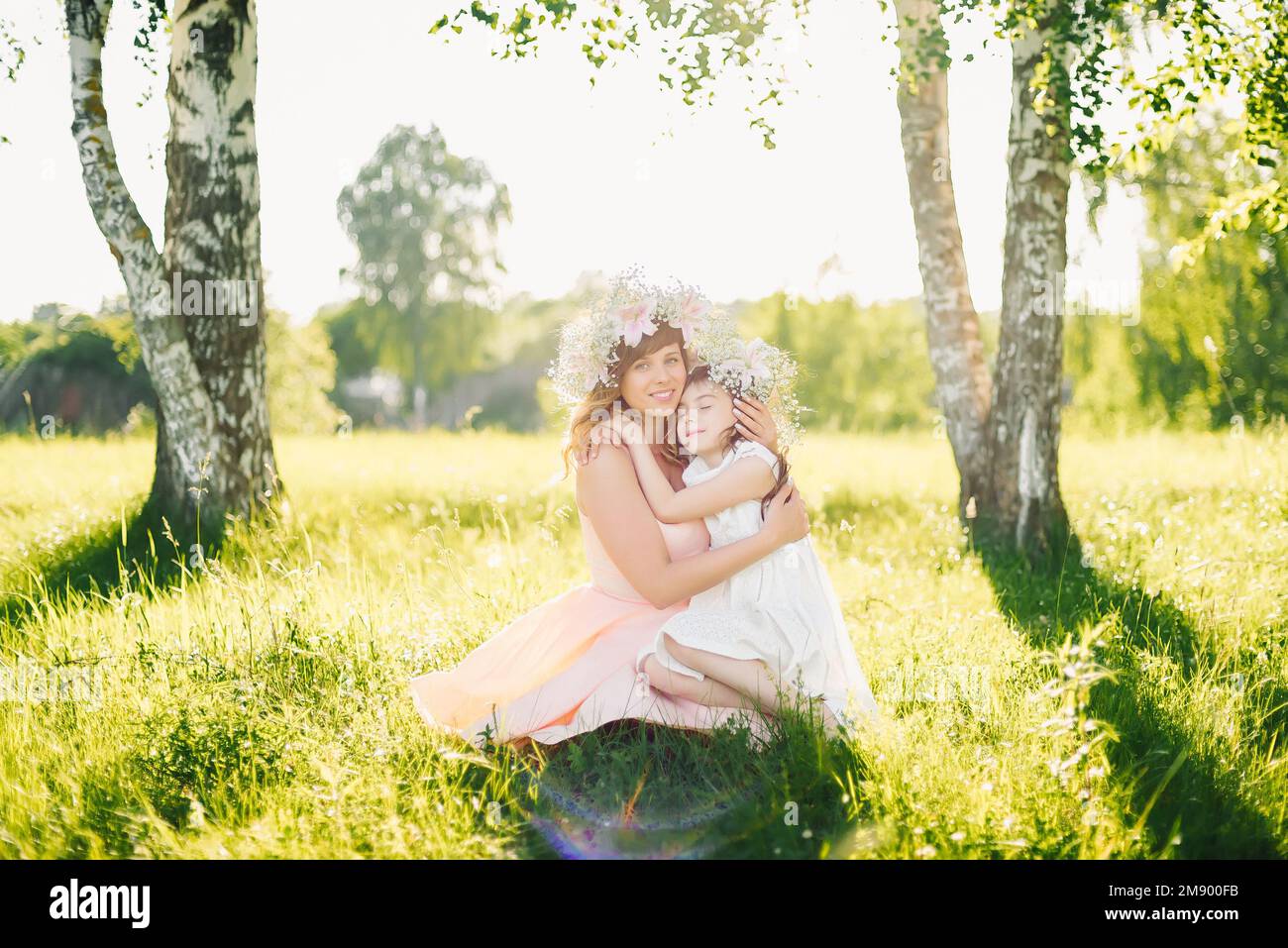 Madre hermosa feliz con una hija de apariencia caucásica abrazándose en el prado en un día de verano Foto de stock