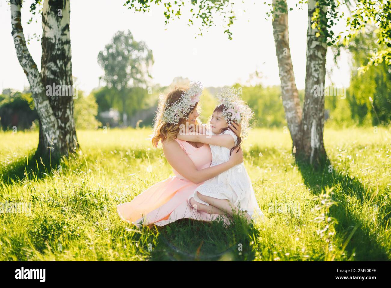 Madre hermosa feliz con una hija de apariencia caucásica abrazándose en el prado en un día de verano Foto de stock