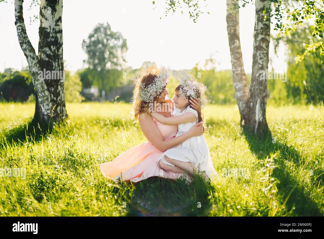 Madre hermosa feliz con una hija de apariencia caucásica abrazándose en el prado en un día de verano Foto de stock