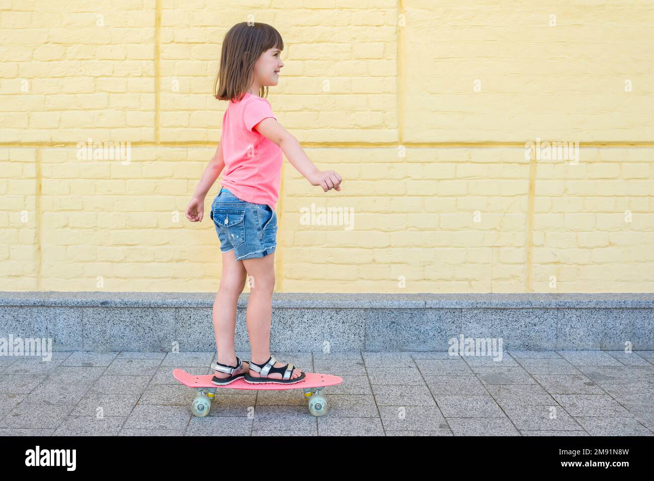 Una niña de 7 a 8 años en una camiseta rosa está patinando en el fondo amarillo de la pared. Estilo de vida Foto de stock
