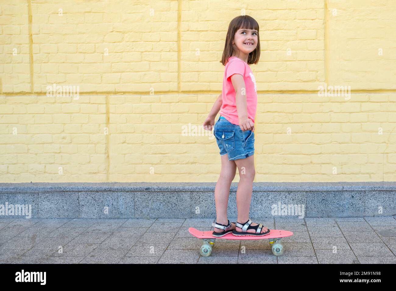Una niña elegante está patinando en el fondo de la pared amarilla. Estilo de vida deportivo Foto de stock