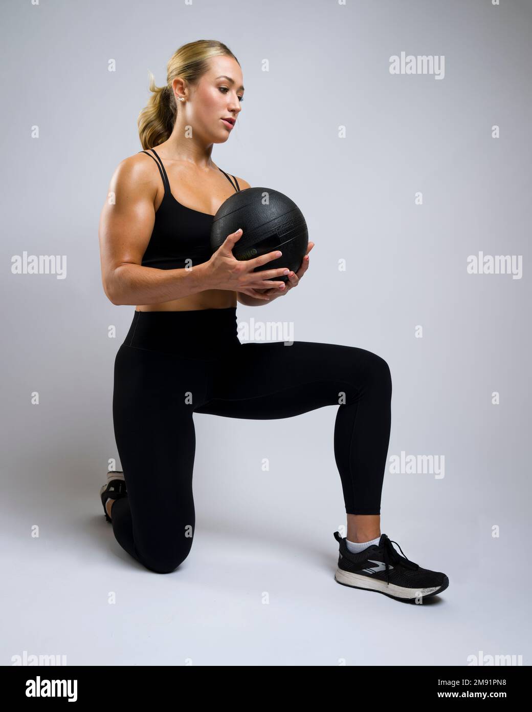 Retrato de la mujer joven musculosa hermosa arrodillada con la bola de la medicina Foto de stock