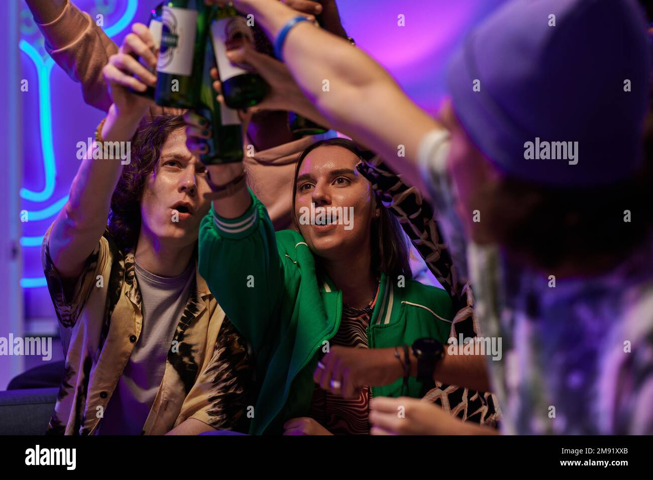 Enfoque selectivo en la joven pareja emocionada con botellas de cerveza brindando con sus amigos mientras celebran la victoria de su equipo de hockey favorito Foto de stock