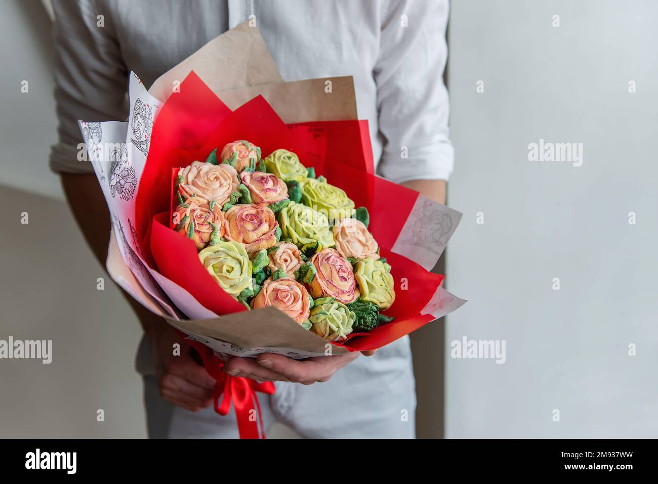 Hombre sin rostro sostiene un ramo de flores dulces de malvavisco en sus  manos. Un regalo en un envoltorio rojo con delicadas rosas de azúcar sobre  un fondo claro. Pequeño Fotografía de