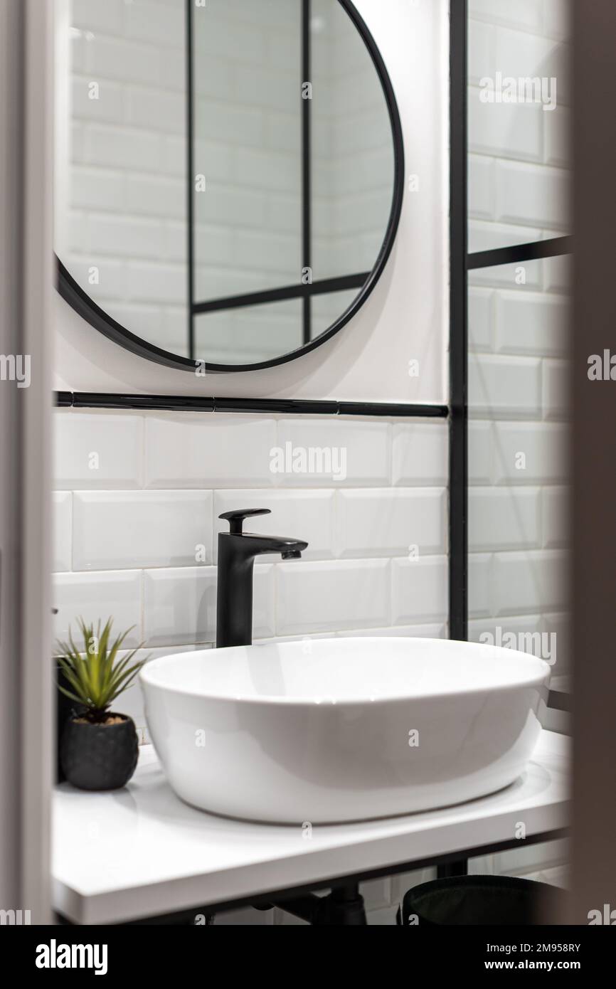Cuarto de baño con paredes de ladrillo blanco, grifo negro, un lavabo  ovalado en una mesa blanca, un espejo redondo en una pared con marcos  negros Fotografía de stock - Alamy