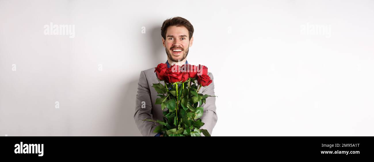 Hombre guapo en el amor deseando feliz día de San Valentín, dando ramo de  flores en la cita romántica, sonriendo en la cámara, traje de vestir sobre  fondo blanco Fotografía de stock -