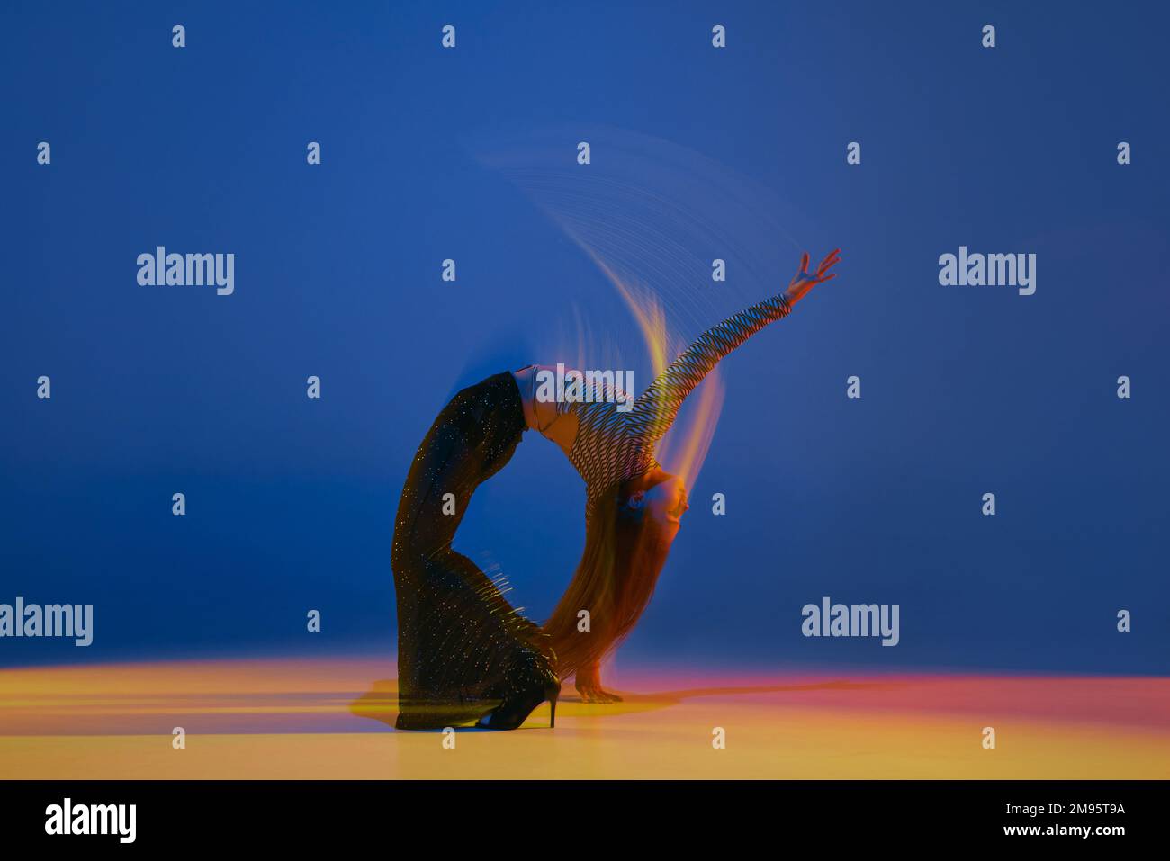 Luces mixtas y flexibilidad. Retrato de la muchacha joven bailando los talones bailan en ropa elegante sobre fondo azul en luz de neón. Concepto de moderno Foto de stock