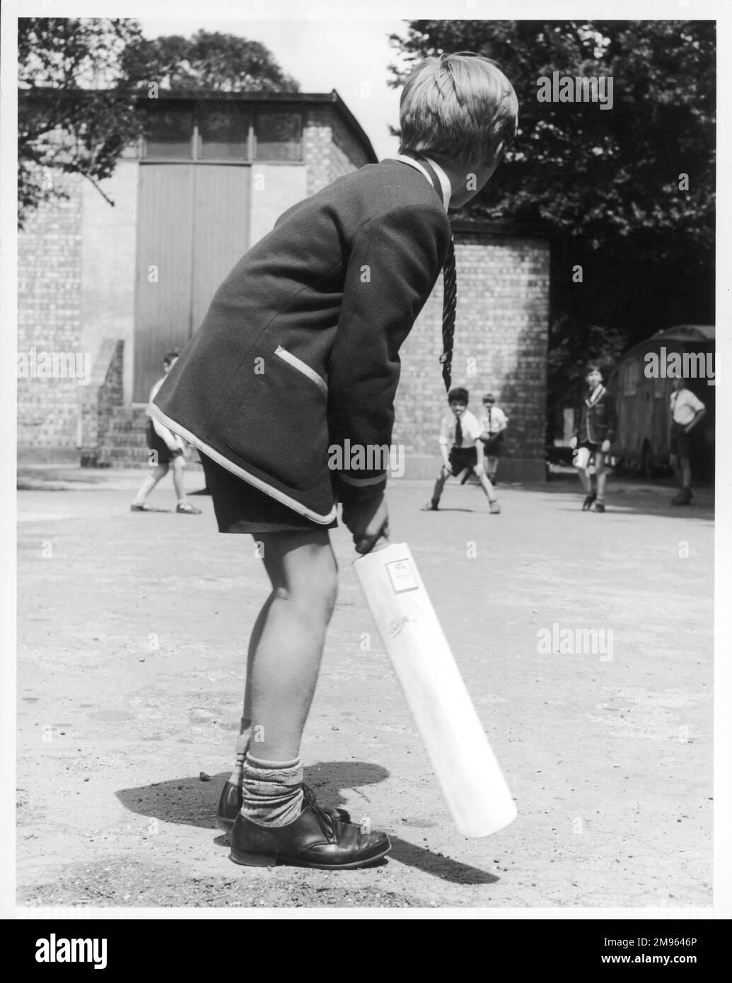Colegiales jugando un juego improvisado de cricket; un niño se prepara para batear Foto de stock