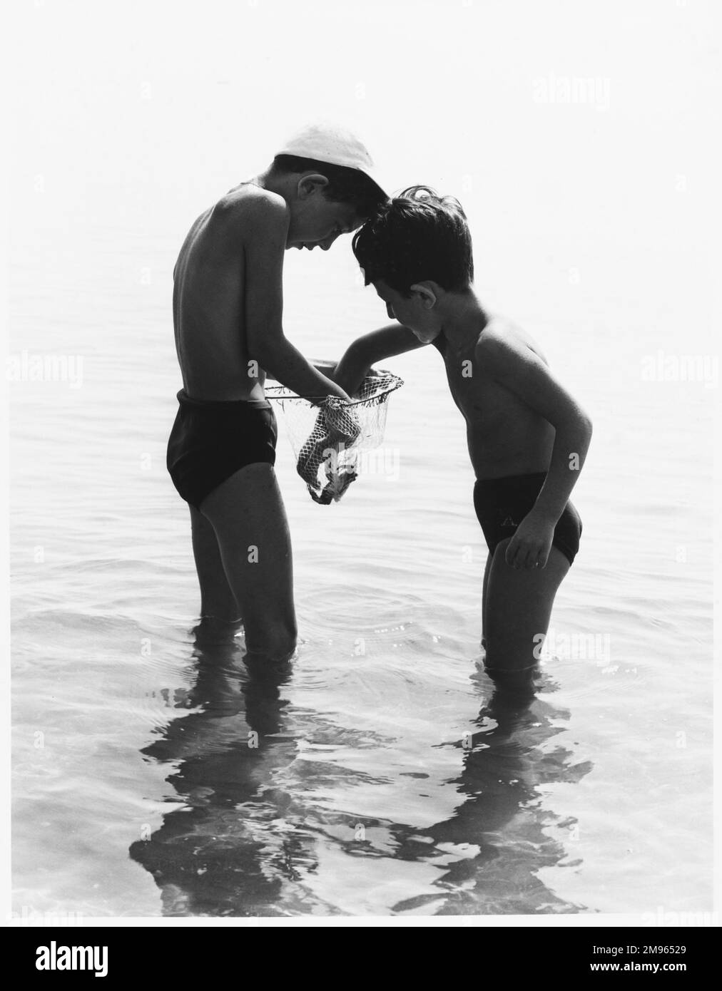 Dos niños se paran en el mar con una red con la que han atrapado un cangrejo. Es mejor que mire sus dedos poniéndolos allí. Foto de stock