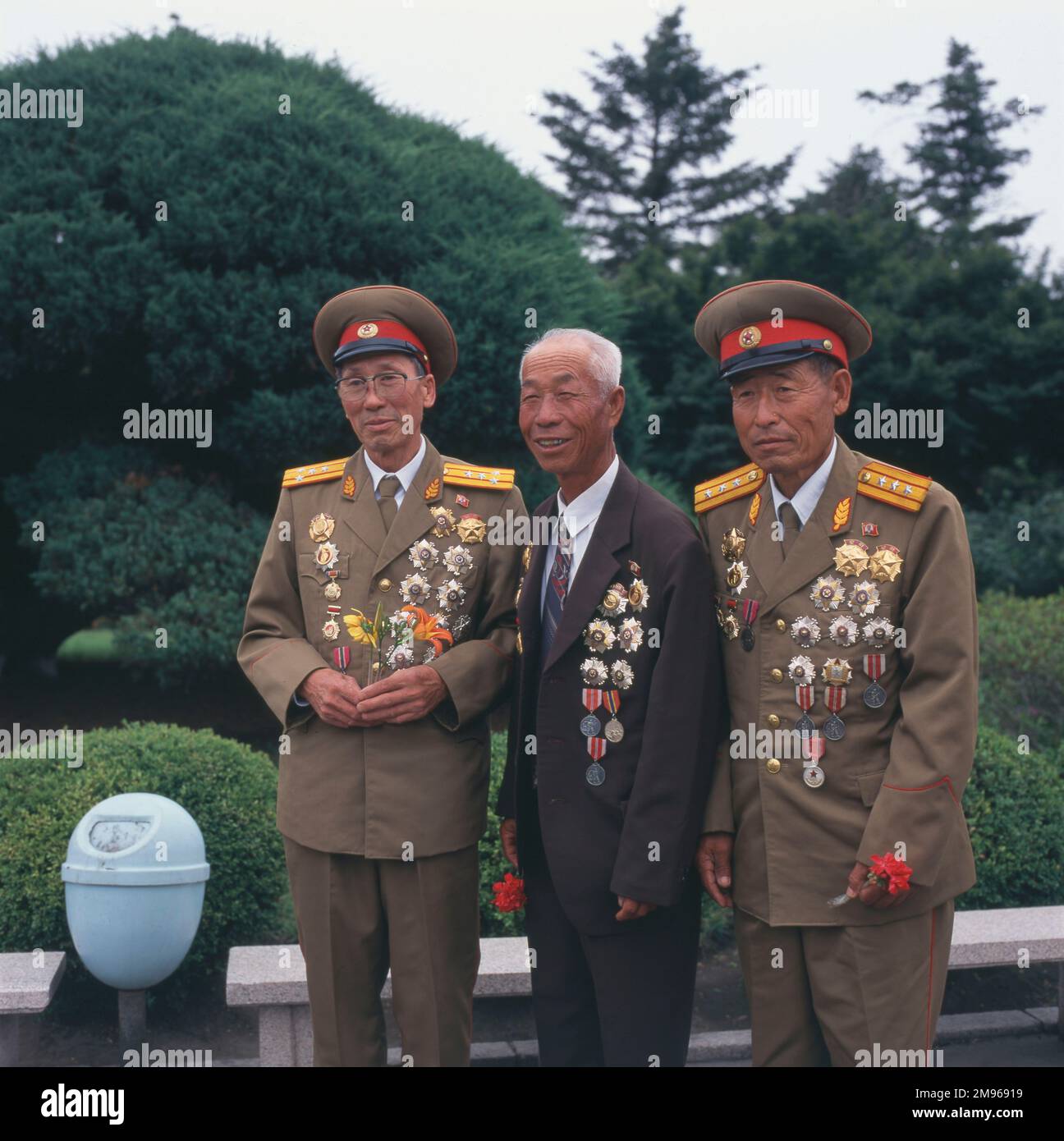 Tres veteranos de la Guerra de Corea (1950-1953) posan para su foto en Pyongyang, capital de Corea del Norte. Dos están en sus uniformes, uno está en un traje, y los tres llevan muchas medallas y decoraciones. Foto de stock