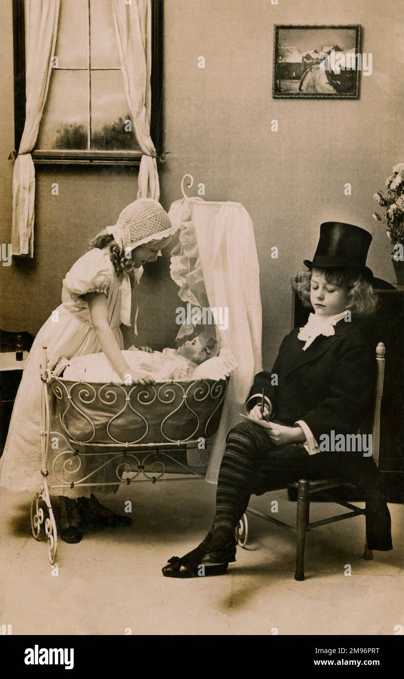 Dos niños pequeños se disfrazan, la niña con un gorro de encaje y un  vestido largo, el niño con sombrero y traje superior, mientras cuidan de su  muñeca bebé Fotografía de stock -