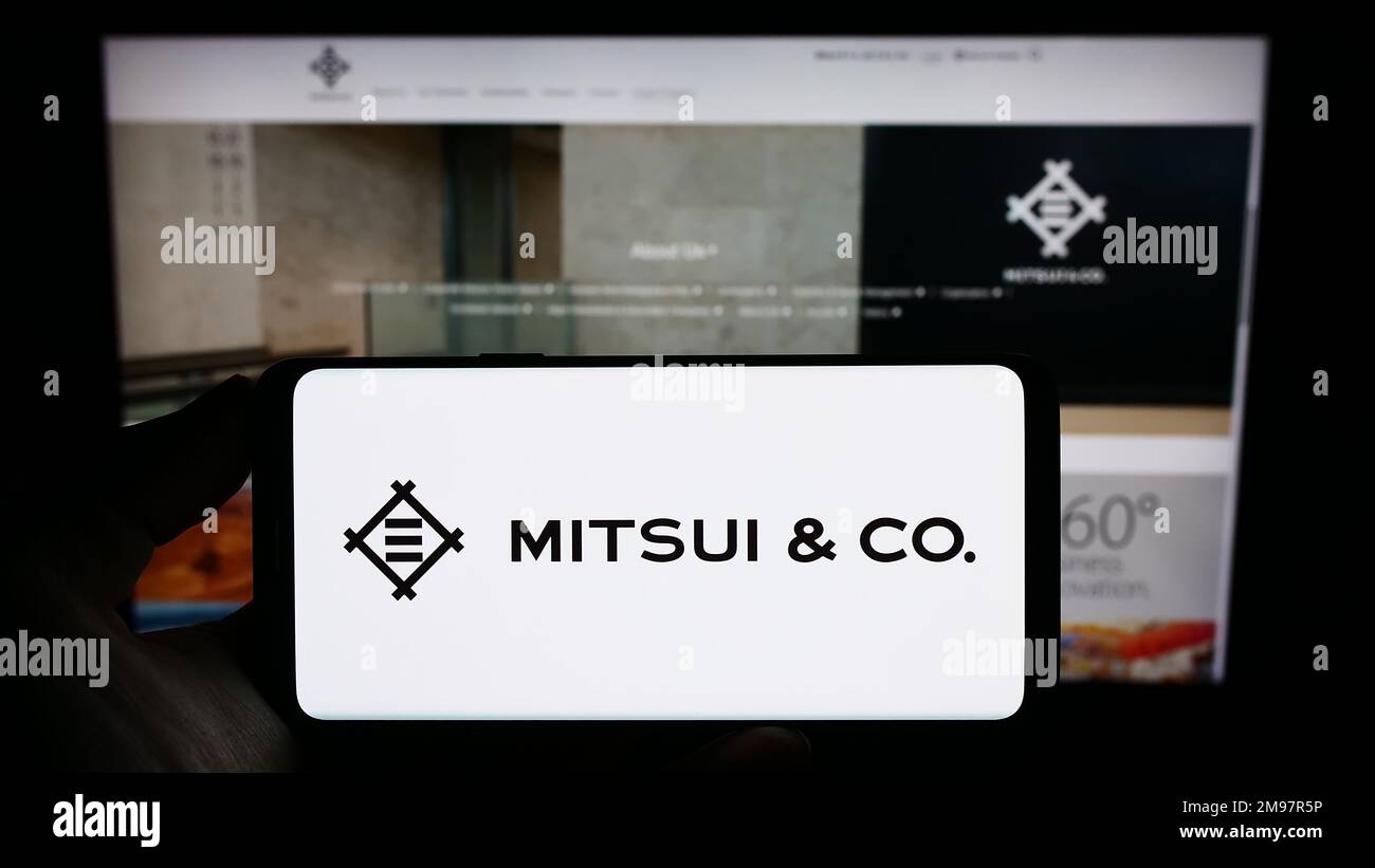 Persona que sostiene el teléfono móvil con el logotipo del conglomerado japonés Mitsui Co. Ltd. En la pantalla frente a la página web de la empresa. Enfoque en la pantalla del teléfono. Foto de stock