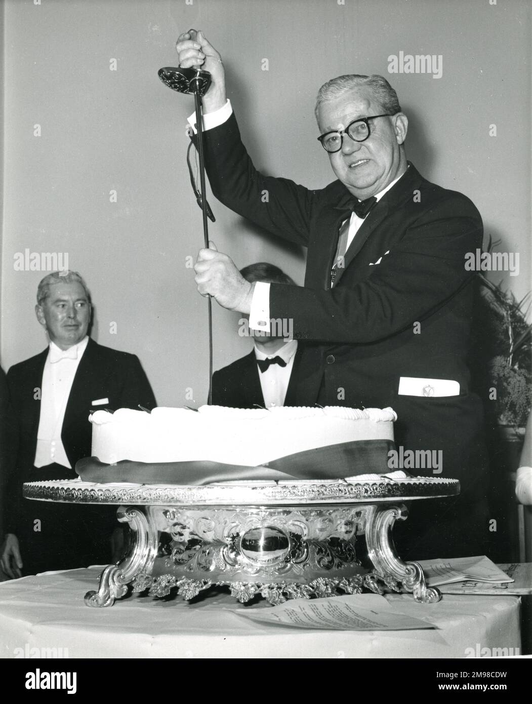 Sir George Gardner, Presidente de Raes 1965-1966, corta el pastel de cumpleaños del centenario con la espada ceremonial que pertenece al General de Brigada Sir Osborne Mance, el miembro más antiguo de la Sociedad, en la Conversación del Centenario celebrada en el Museo de Ciencias el 12 de enero de 1966. Foto de stock