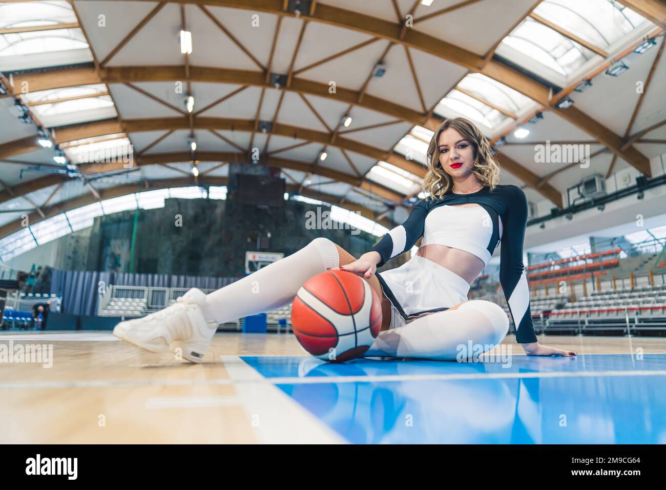 Tiro completo de ángulo bajo de una animadora sentada en el suelo con un baloncesto. Concepto deportivo. Foto de alta calidad Foto de stock