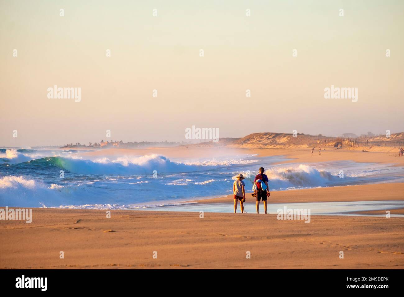 Todos Santos, Baja California, México, una pareja caminando en la playa al lado del surf grande