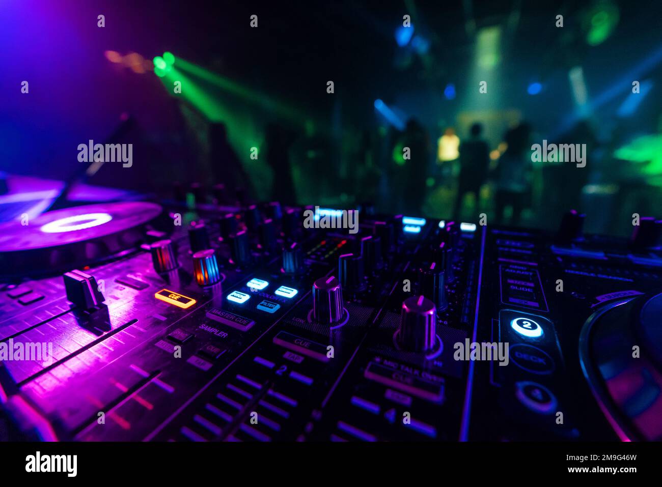 Tablero del regulador del mezclador de DJ para la mezcla profesional de la música electrónica en un club nocturno en una fiesta con gente bailando en el fondo Foto de stock