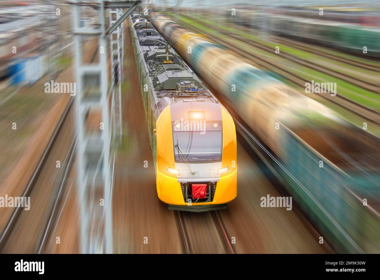 Tren eléctrico amarillo suburbano con coches de pasajeros se precipita a lo largo de la vía del ferrocarril, vista aérea Foto de stock