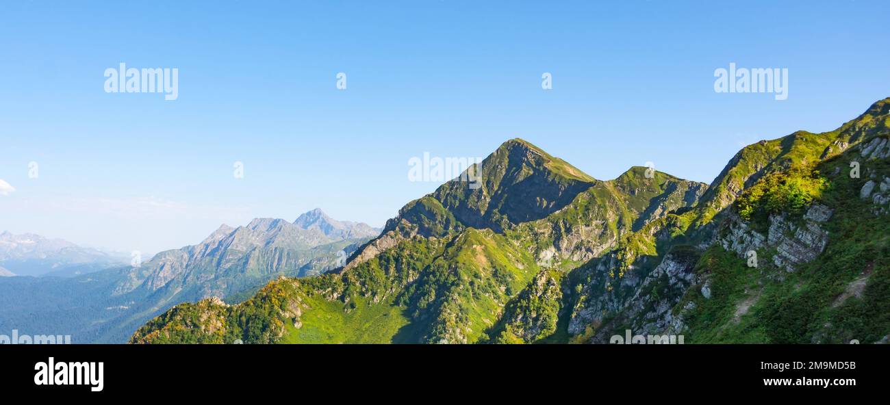 Panorama de una cadena montañosa con gargantas sombreadas y prados alpinos en las laderas, otras montañas en la distancia Foto de stock