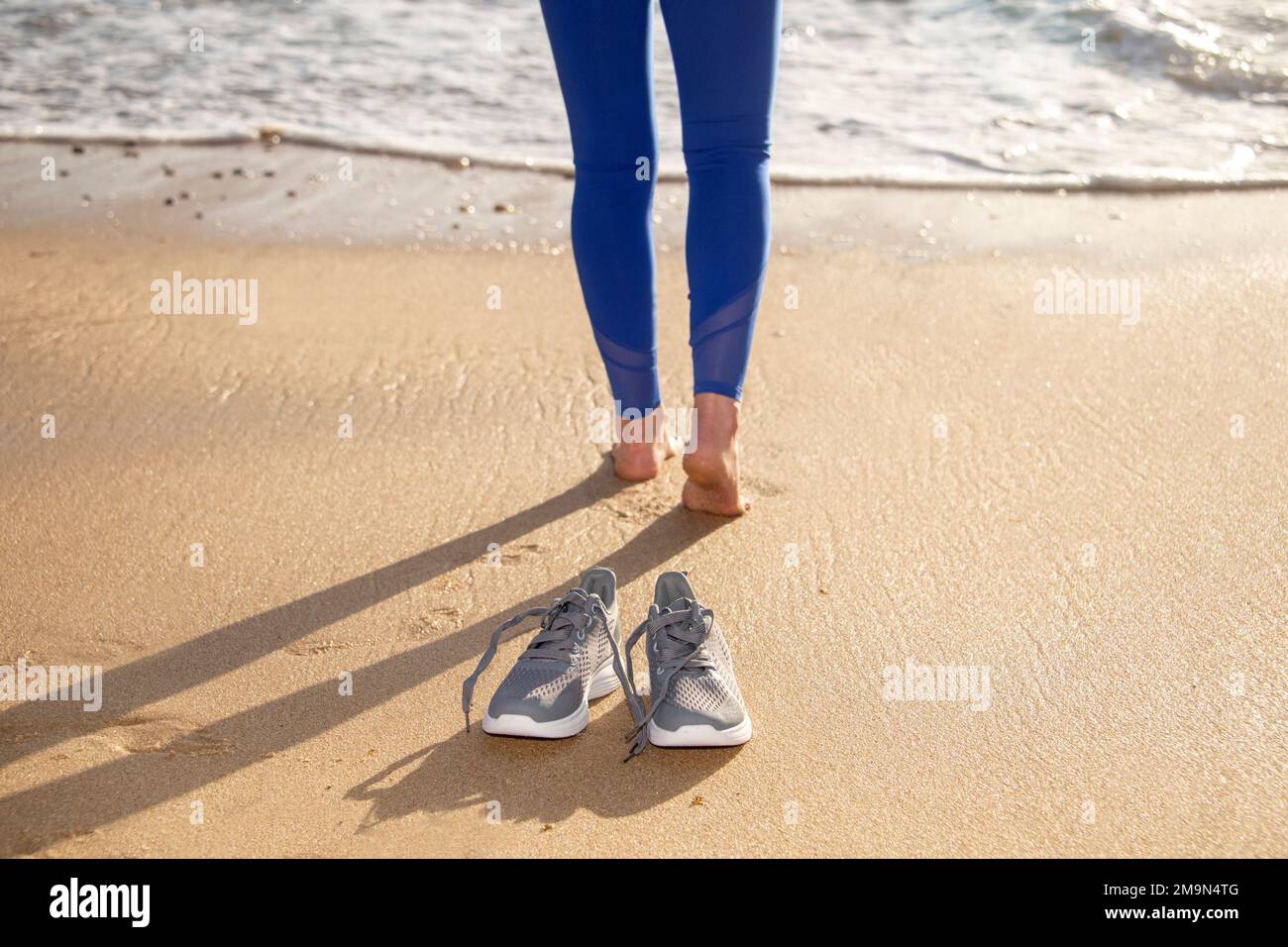 Mujer caminando descalza en la playa, zapatos en foco, poco profundo DOF Foto de stock