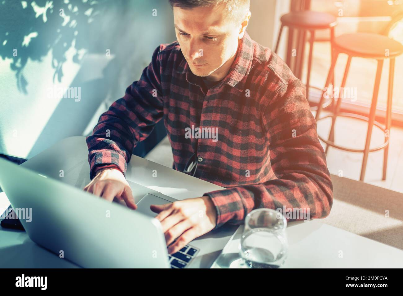 Alegre freelancer usando laptop sentado en la mesa en el café en día soleado. Foto de stock