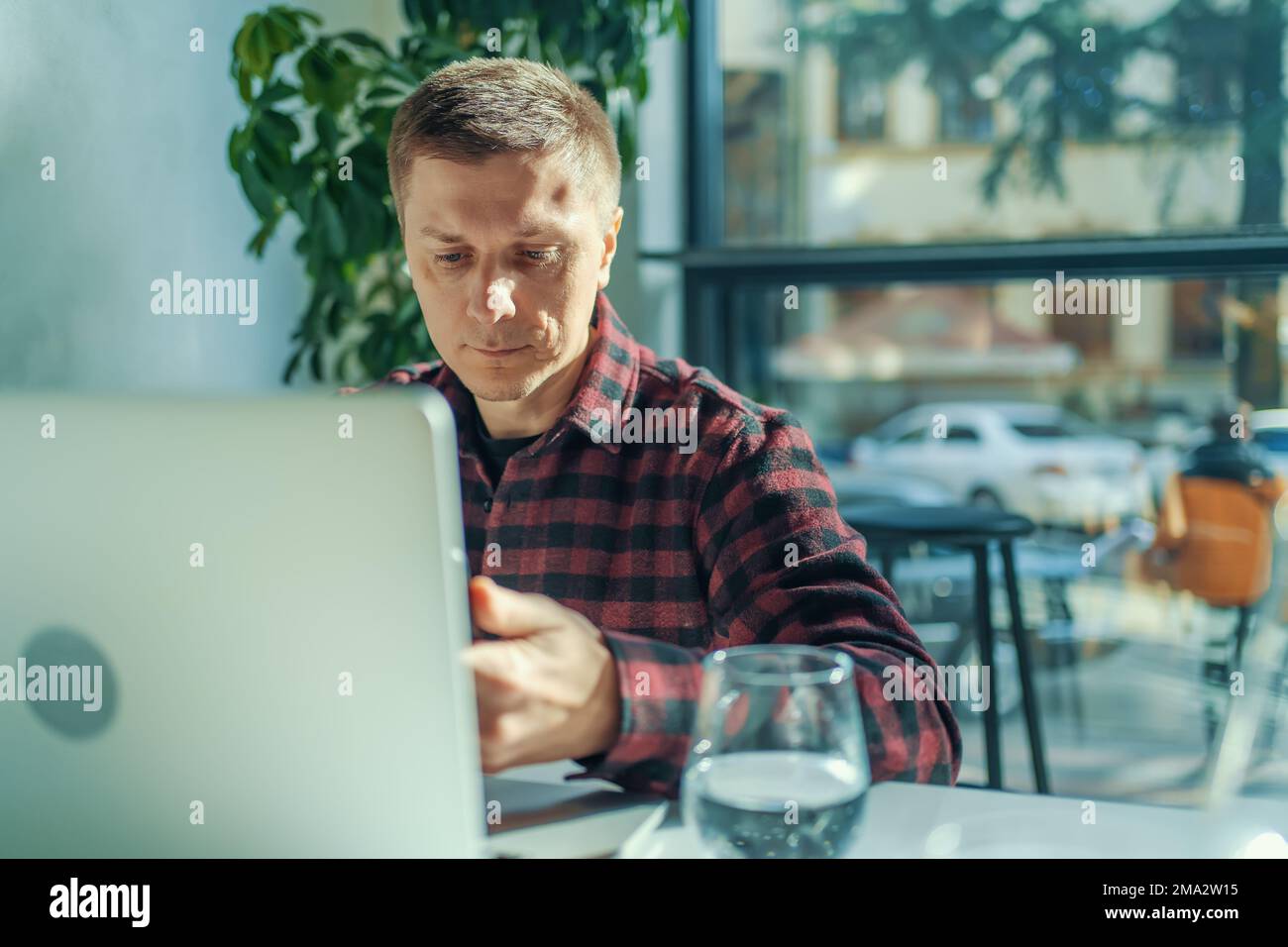 Alegre freelancer usando laptop sentado en la mesa en el café en día soleado. Foto de stock