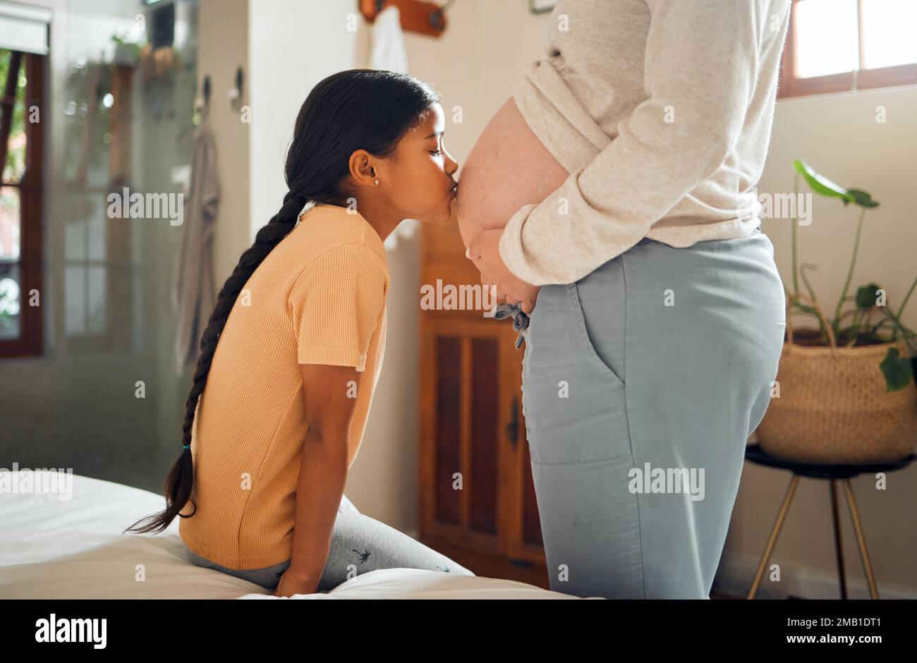 Embarazada, familia y amor con una niña besando el vientre de su madre mientras se une en el dormitorio de su casa. Niños, mamá y embarazo con un beso Foto de stock