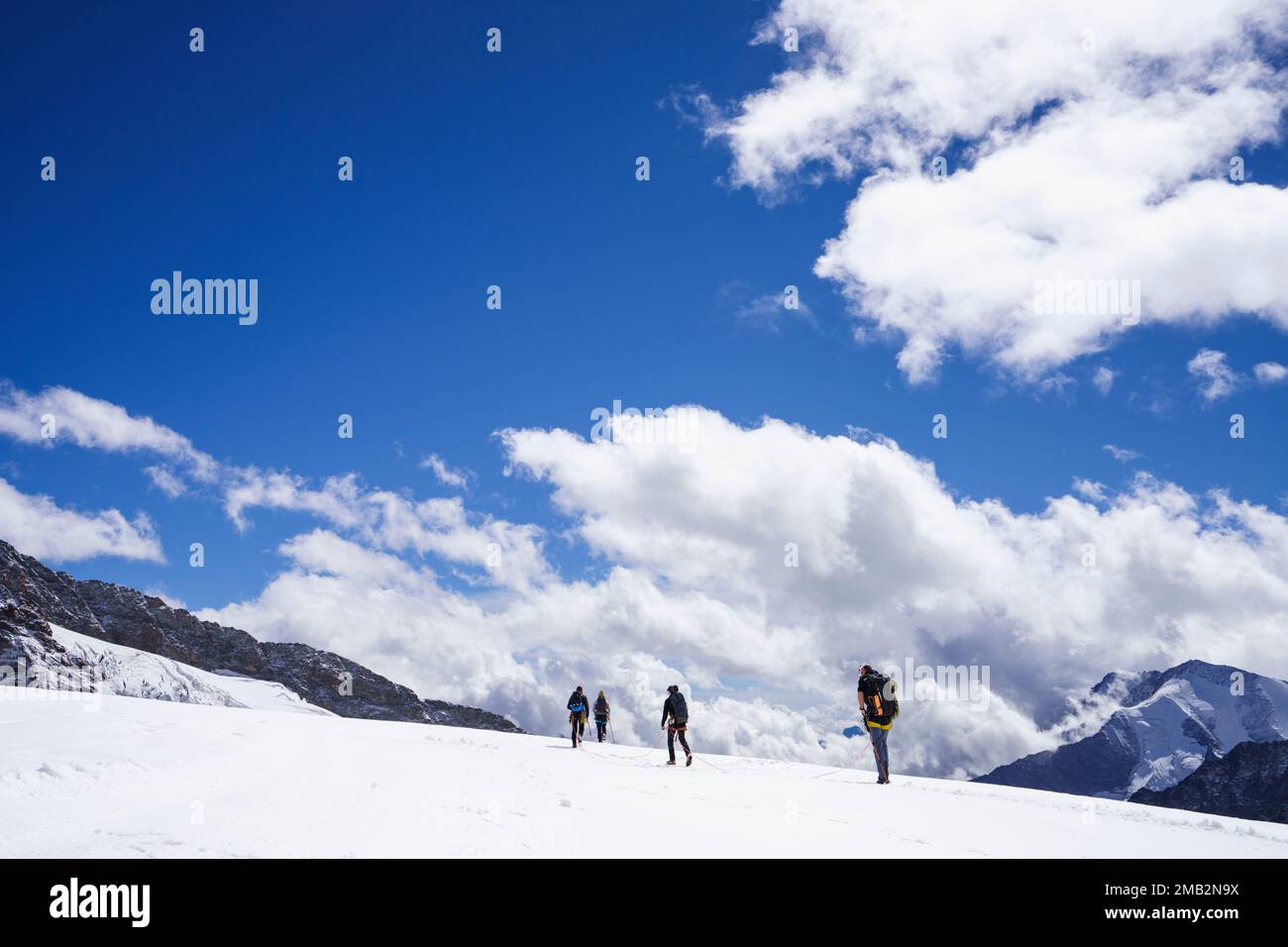 Excursionistas alpinos glaciares de senderismo en el glaciar Aletsch. Los montañeros caminan en la cima del glaciar contra las montañas, cielo azul con nubes. alpes suizos, Jung Foto de stock