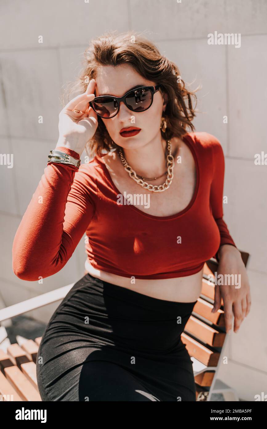 Retrato de moda de mujer hermosa en camiseta negra y falda roja caminando  en el parque. accesorios de gafas de ropa de moda. concepto de venta  comercial
