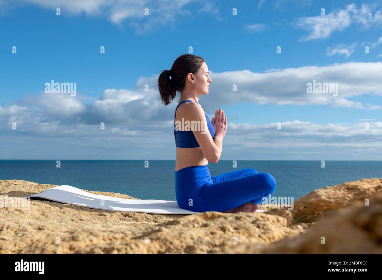 Mujer en forma meditando por el océano, sentado en una estera de yoga. Foto de stock