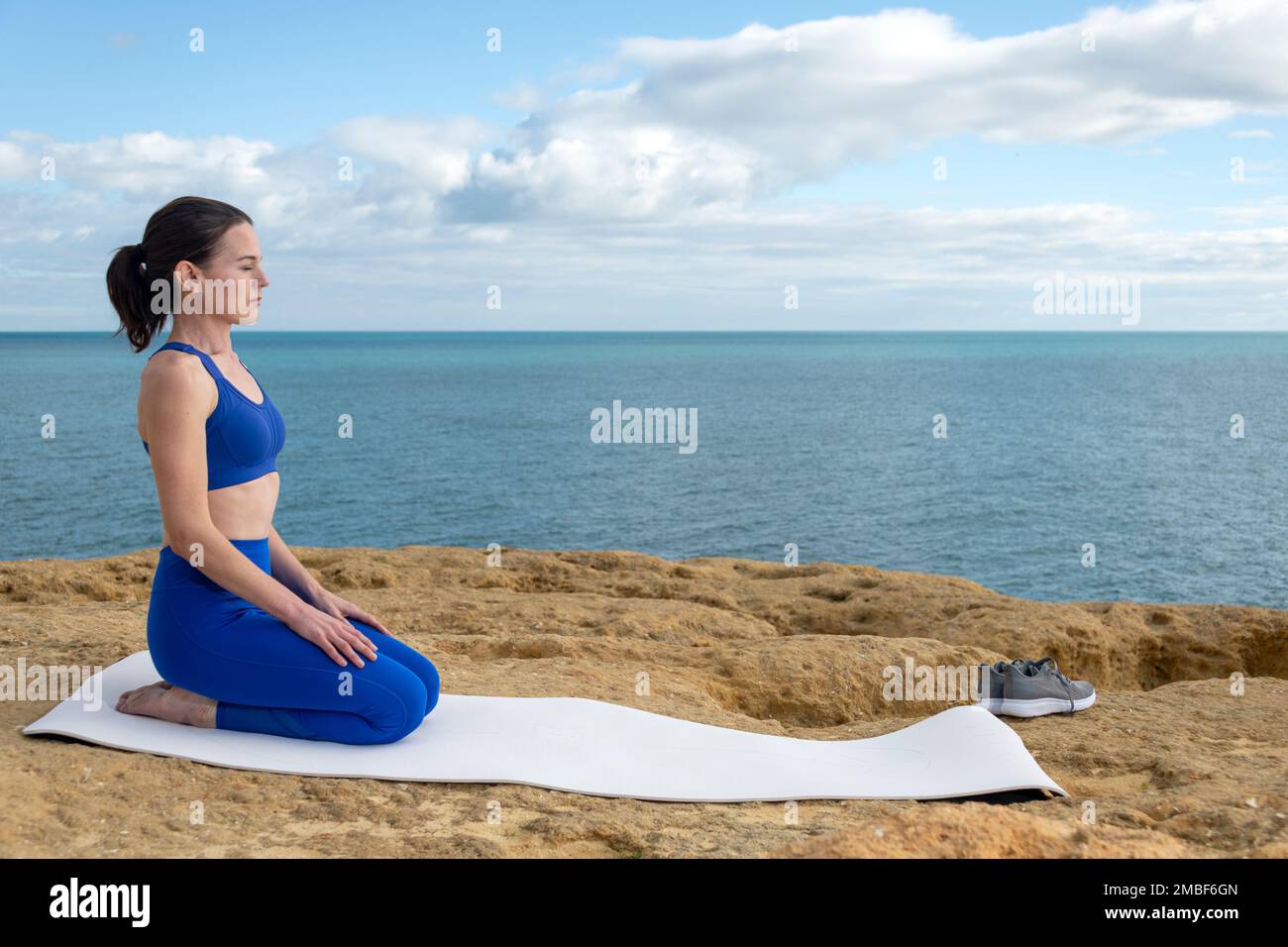 Ajuste mujer arrodillada en un yoga, estera de ejercicio junto al océano. Foto de stock