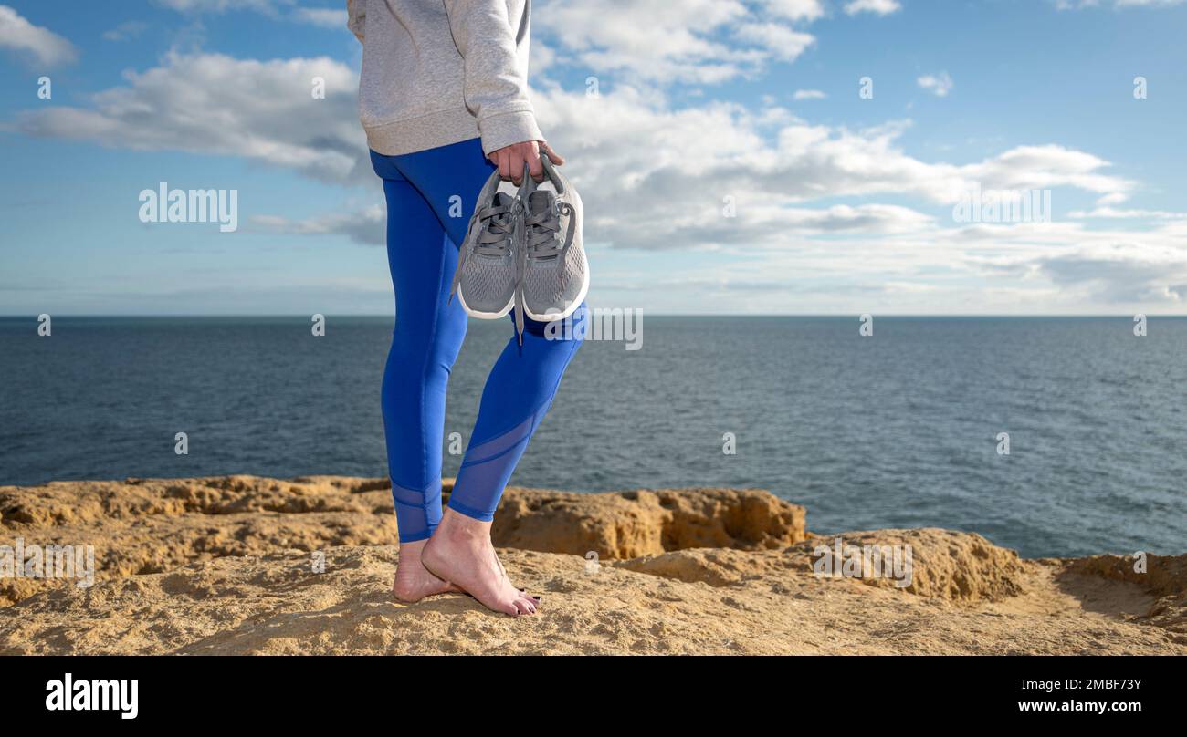 Mujer deportiva descalza llevando sus entrenadores por el océano, de cerca. Foto de stock