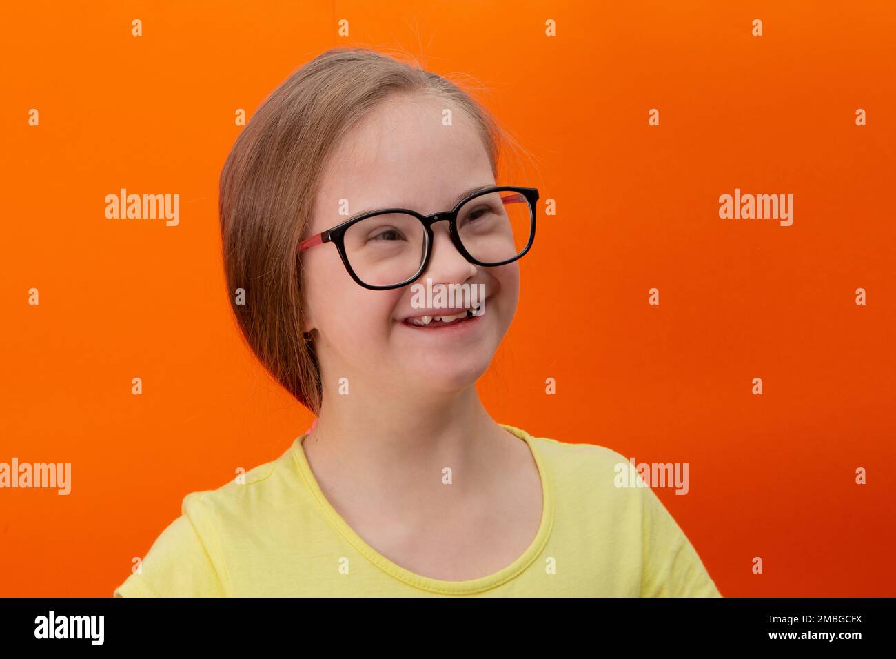 Chica feliz con síndrome de Down. Divirtiéndose, riendo. Coletas divertidas. Estudio. Retrato sobre fondo naranja Foto de stock