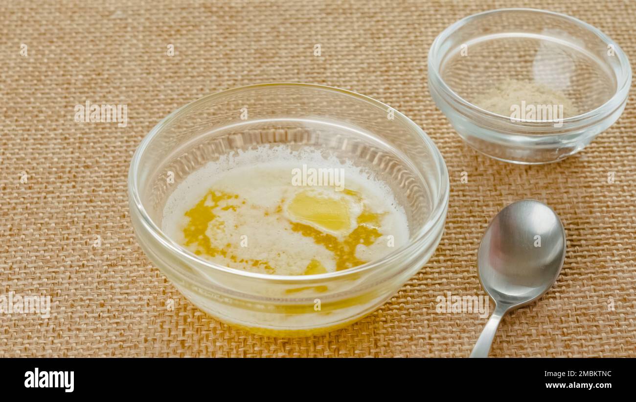 Mantequilla derretida en un tazón de vidrio y condimento de ajo en un tazón de vidrio de cerca en una mesa de cocina Foto de stock