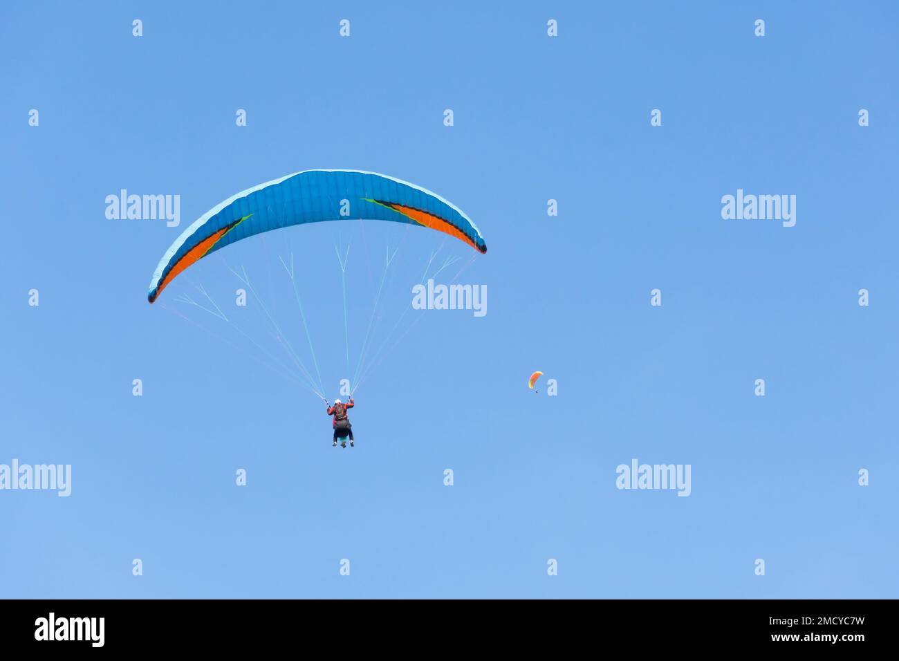Dos parapente en tándem vuelan contra el cielo azul, parapente en tándem a distancia guiado por un piloto Foto de stock