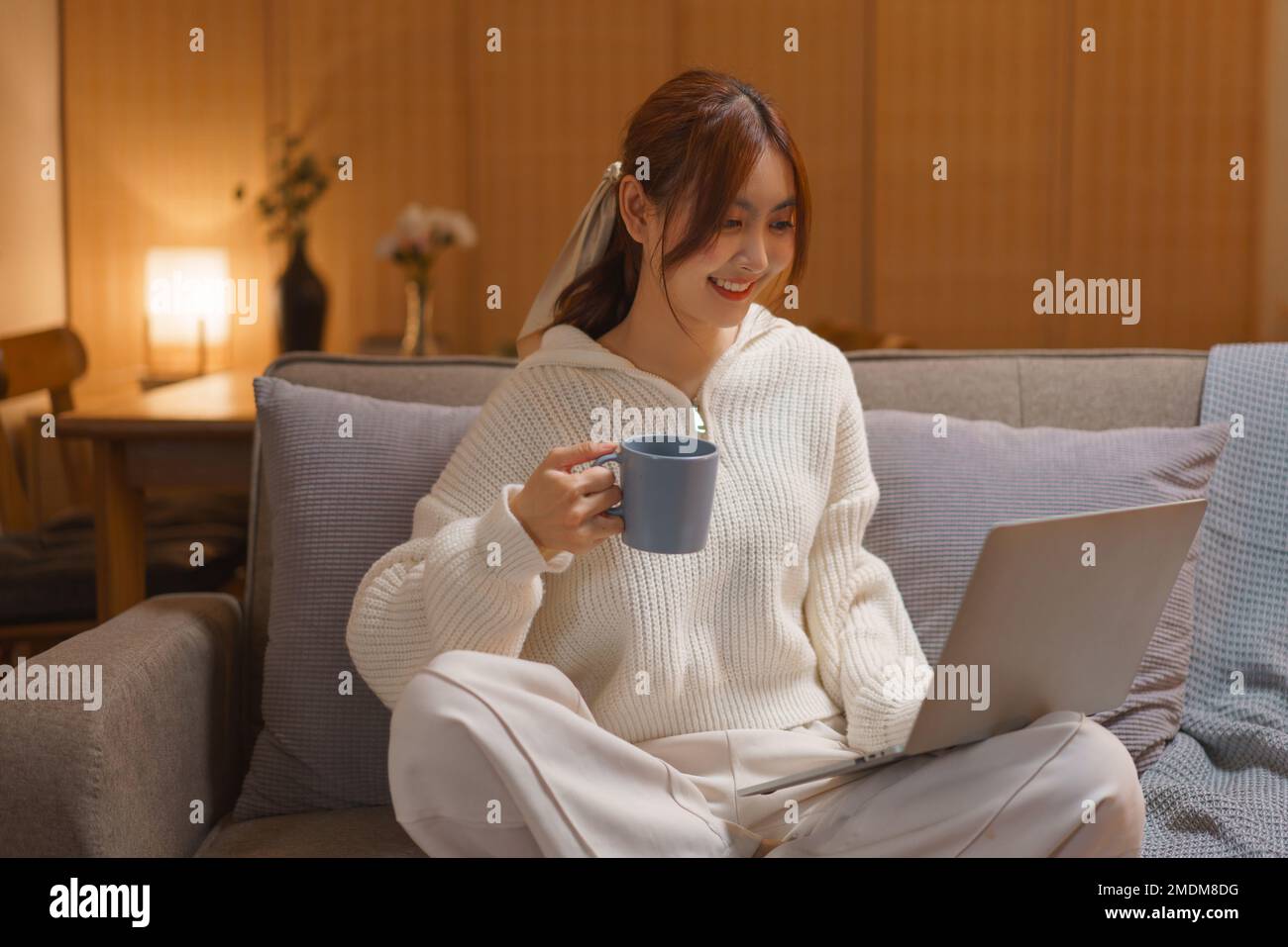 Concepto de estilo de vida en casa, mujer joven bebe té y ve la película en la computadora portátil en la noche en invierno. Foto de stock