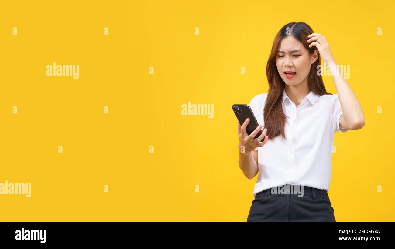 Las mujeres se sienten confundidas mientras leen datos en el teléfono inteligente con espacio vacío sobre fondo amarillo aislado. Foto de stock