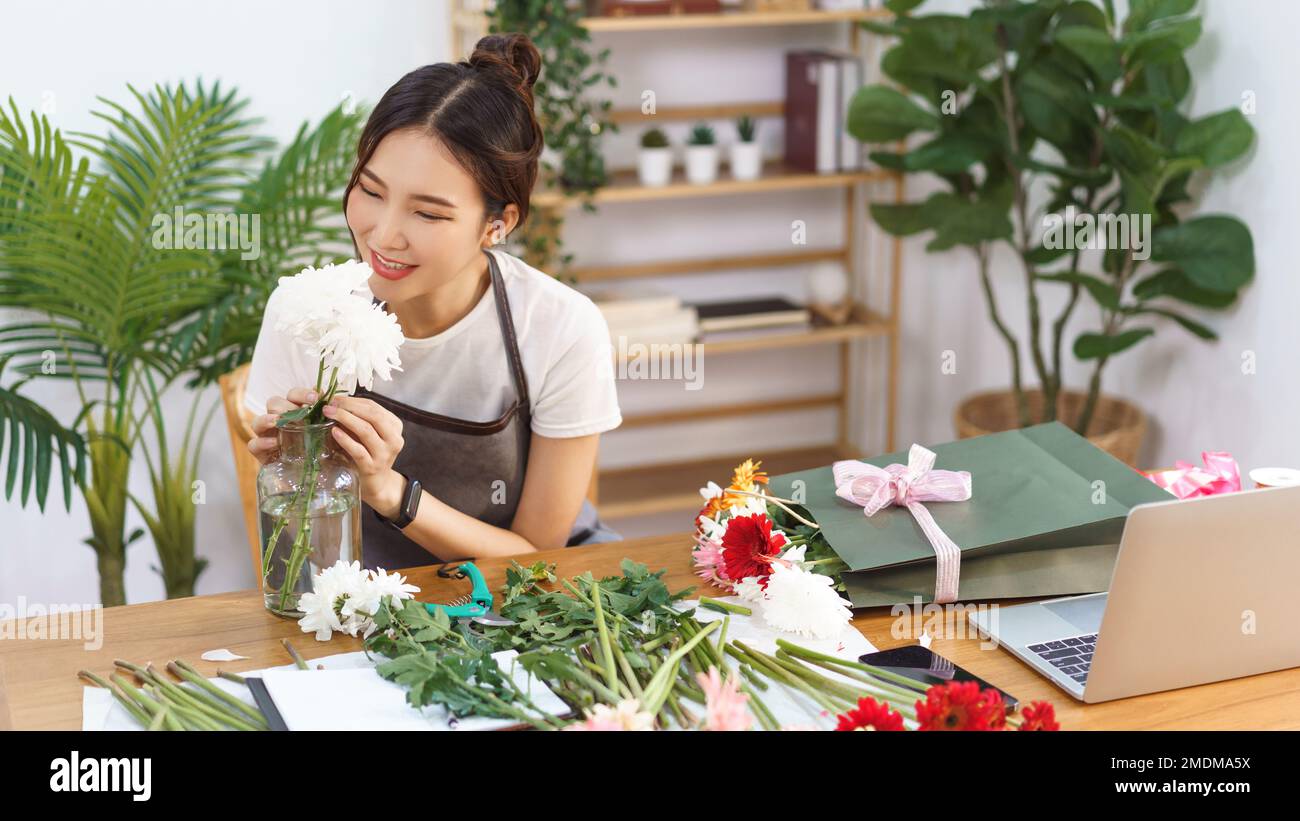 Concepto de floristería, Florista femenina sonrisa y olores de crisantemos blancos en florero con felicidad. Foto de stock