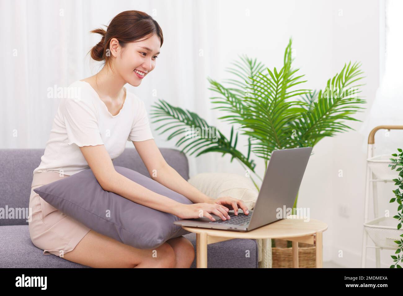 Estilo de vida en el concepto de sala de estar, mujer joven asiática sentada en el sofá y escribiendo en el portátil. Foto de stock