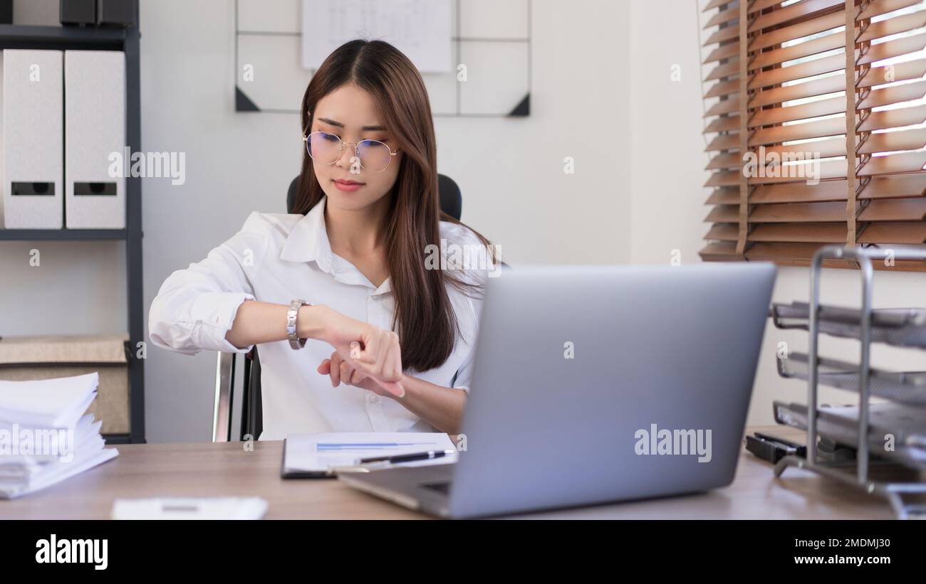 Concepto de negocio, businesswoman es mirada en el momento en el reloj de pulsera después de trabajar duro en la oficina. Foto de stock