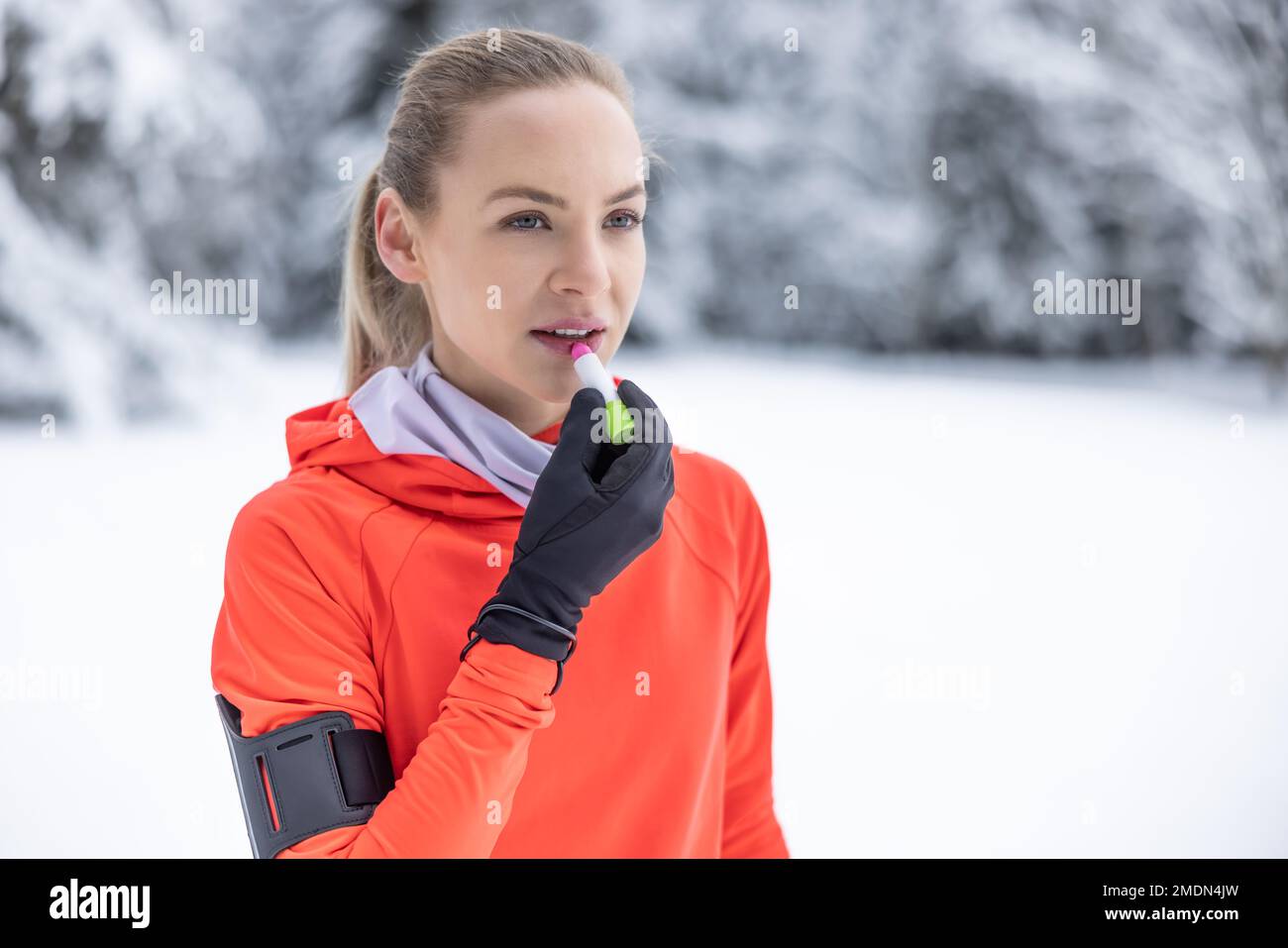 Una joven corredor aplica bálsamo protector a sus labios debido al clima helado, la prevención de labios agrietados y secos. Foto de stock