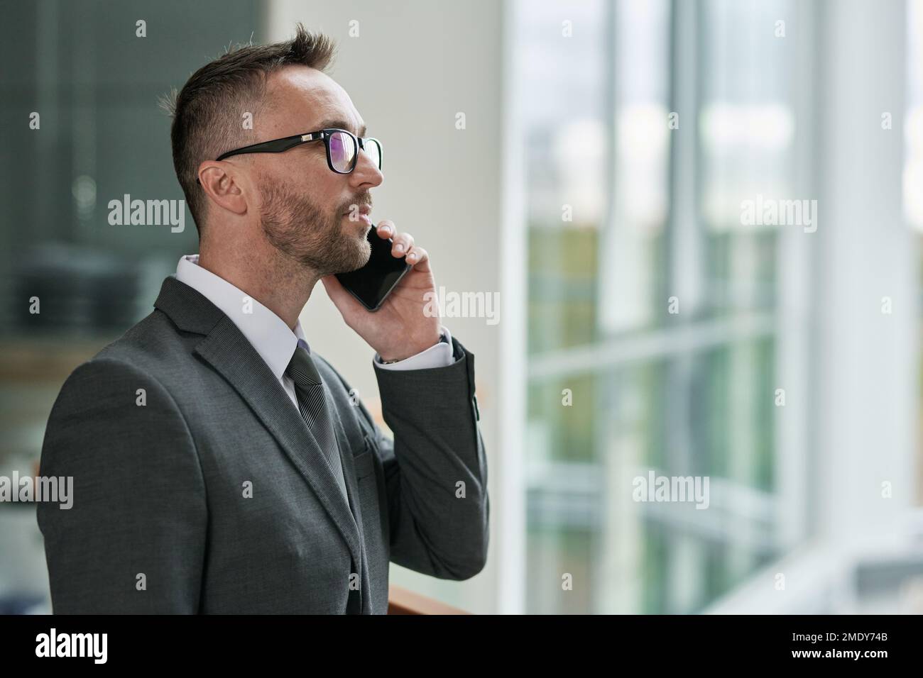 Vista lateral del joven director confiado de la empresa de negocios hablando con uno de sus subordinados en el teléfono inteligente frente a la cámara Foto de stock