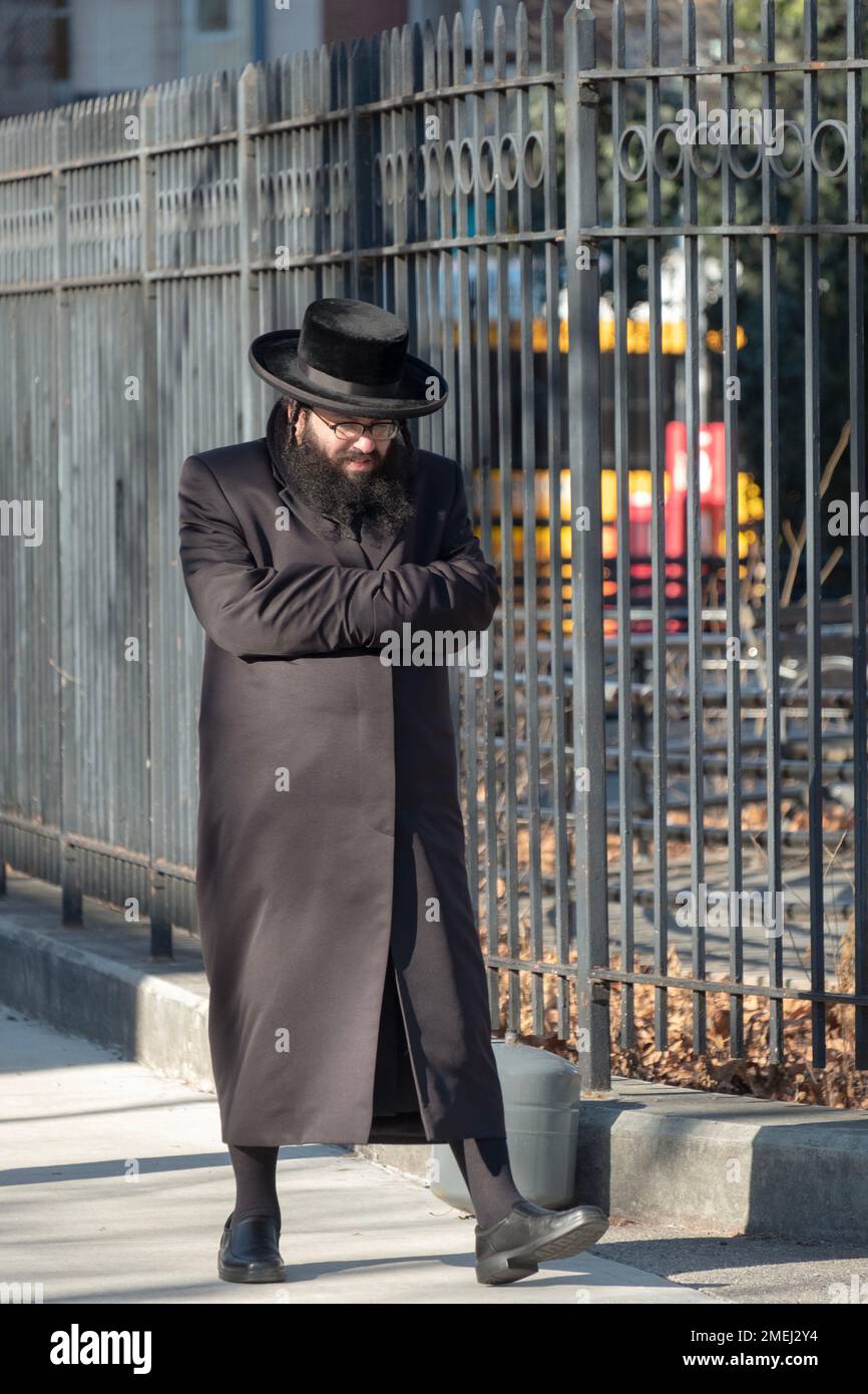 Un hombre jasídico caminando en un frío día de invierno y usando sus mangas de abrigo como guantes. ¡No es una pose poco común! En Brooklyn, Nueva York. Foto de stock
