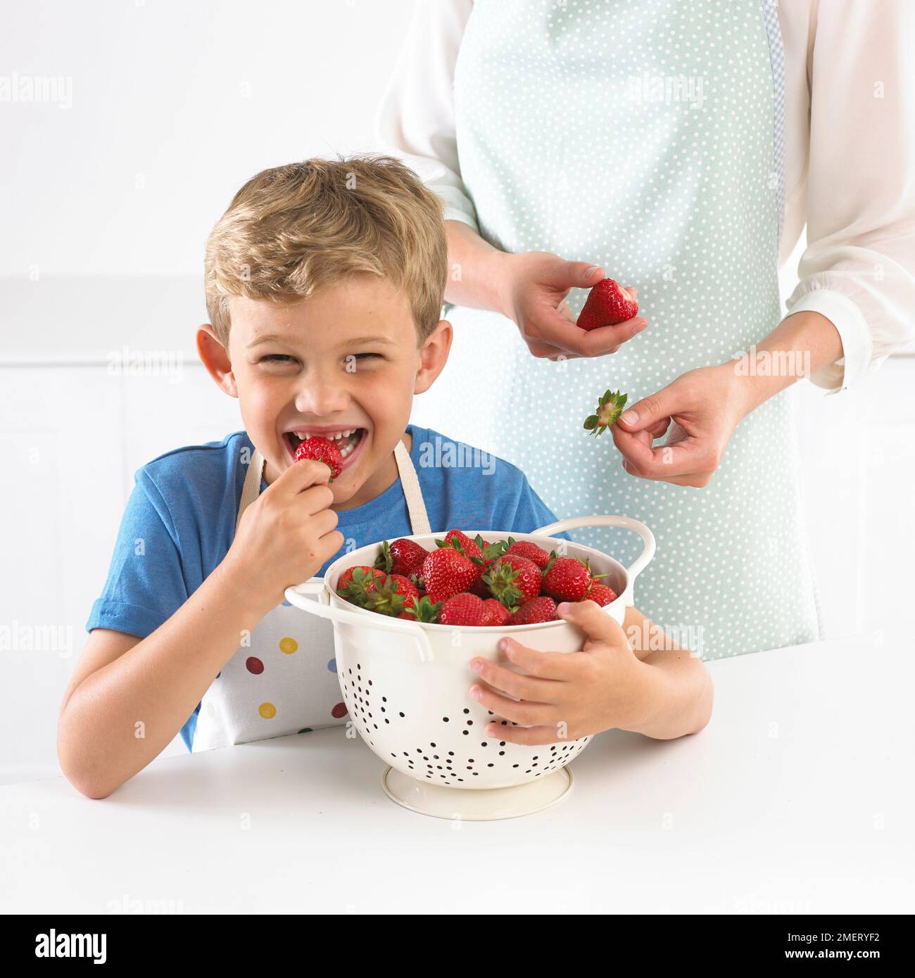 Niño sosteniendo un colador lleno y comiendo una fresa, 6 años Foto de stock