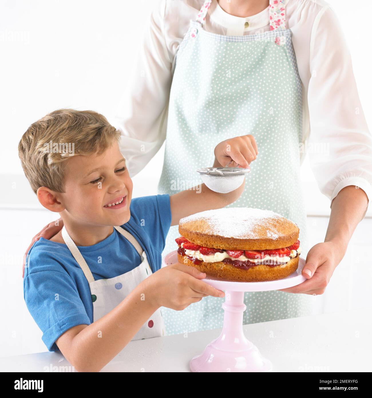 Niño tamizando azúcar glaseado en esponja de fresa, 6 años Foto de stock