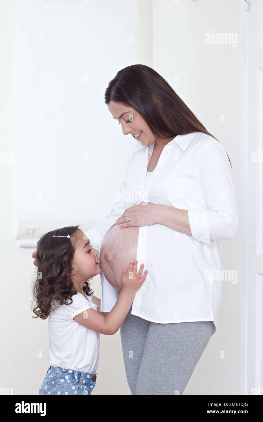 Niña (3,5 años) besando el vientre embarazada de su madre Foto de stock